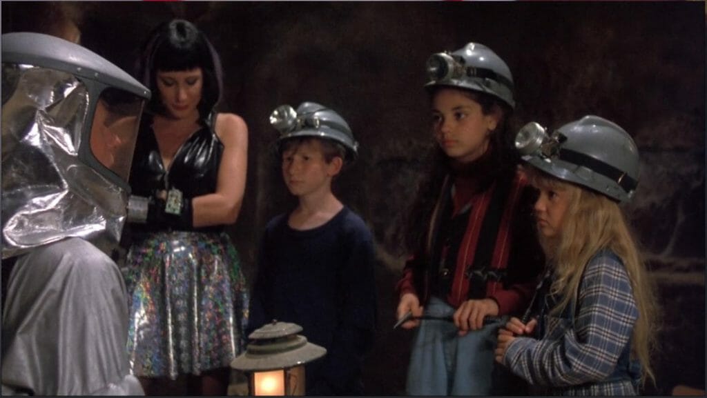 The three kids from the movie wearing hard hats in a catacomb.